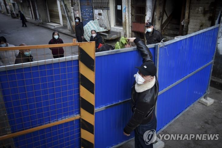 중국 후베이성 우한에서 마스크를 쓴 한 남성이 주택단지 봉쇄를 위해 설치된 바리케이드 너머로 식료품을 전달하고 있다. [AP=연합뉴스 자료사진]