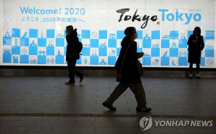일본 도쿄 신주쿠역 근처의 도쿄올림픽 광고 표지판 앞을 걷는 사람들의 모습. [로이터=연합뉴스]
