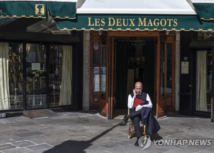 15일(현지시간) 신종 코로나바이러스 감염증(코로나19) 여파로 문을 닫은 프랑스 파리의 대표적 카페 '레 두 마고'(Les Deux Magots) 앞에 한 남성이 앉아 있다. 에두아르 필리프 프랑스 총리는 이날 코로나19 확산 방지를 위해 전국의 음식점과 카페 등 비필수 상점들을 15일부터 당분간 폐쇄한다고 발표했다. / 연합뉴스