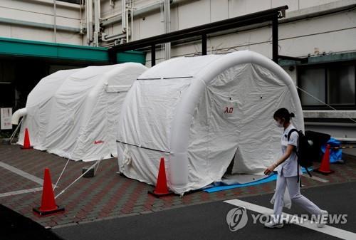 19일 일본 도쿄도(東京都)의 한 병원에서 의료 당국자들이 신종 코로나바이러스 감염증(코로나19) 검사용 텐트 근처를 지나고 있다. / 연합뉴스